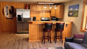 A compact kitchen with wooden cabinets, a refrigerator, a stove, and bar stools.