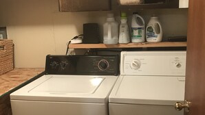 A laundry area with two washing machines, a shelf with cleaning supplies, and a wooden cabinet above.