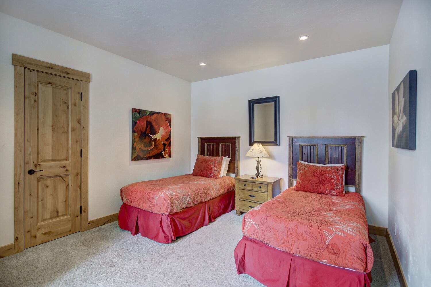 A bedroom with two single beds, a wooden door, a painting, a mirror, and a dresser.
