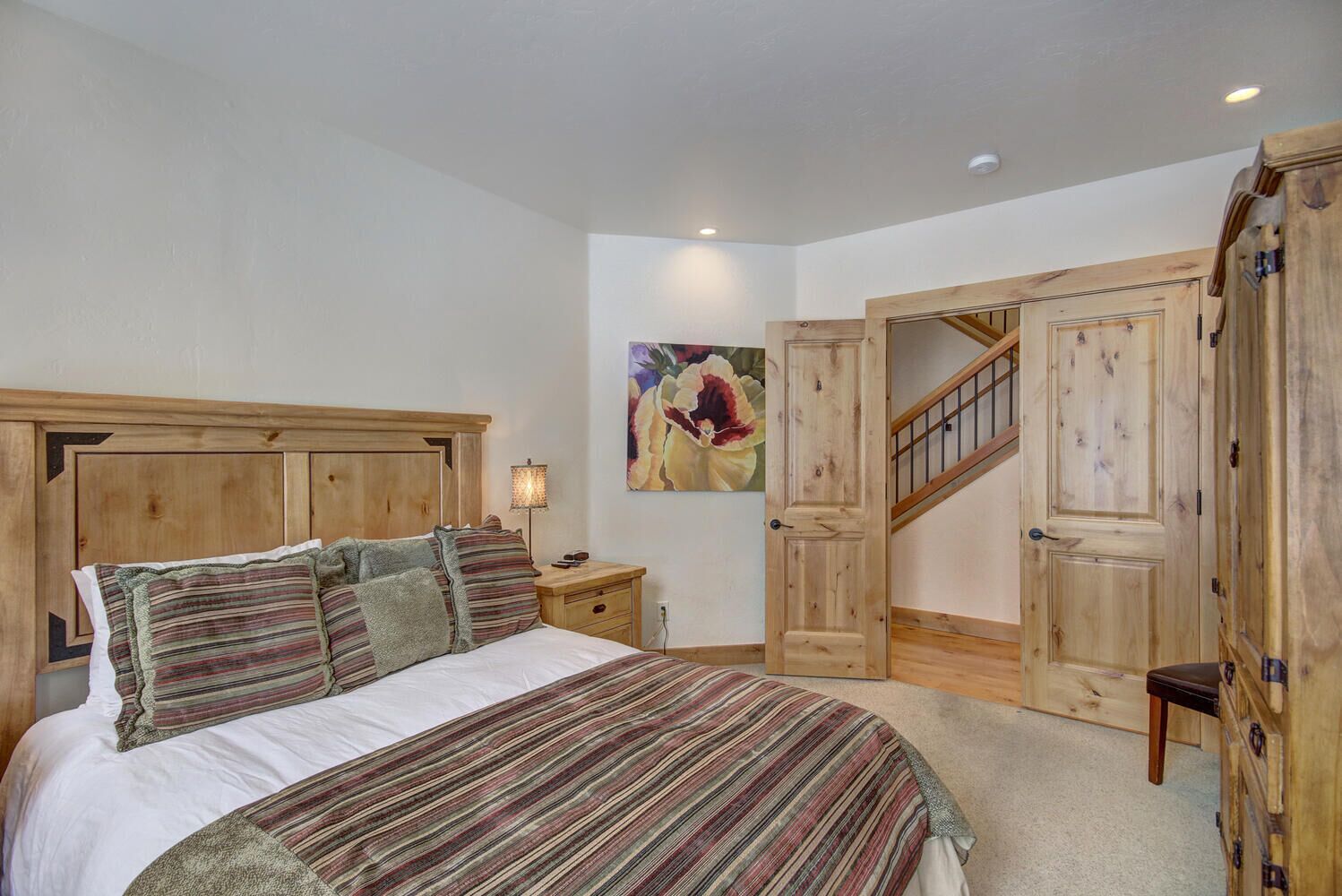 Ein Schlafzimmer mit einem großen Bett, einem Holzkopfende, einem Nachttisch, einem Gemälde und einer Holztreppe.