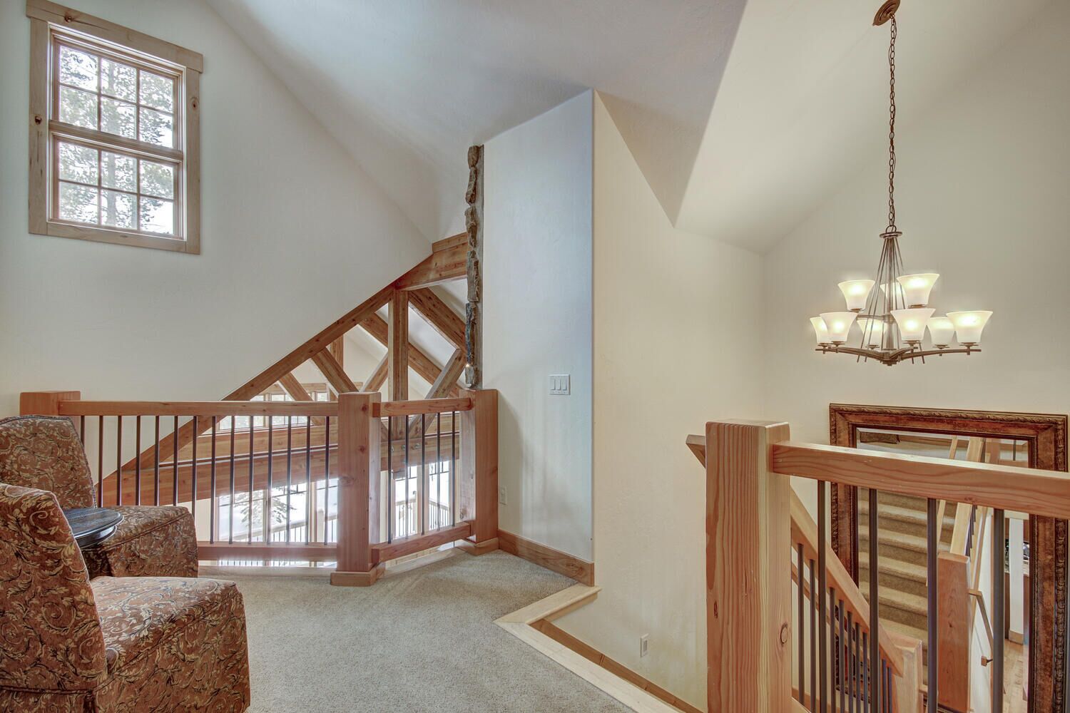 A spacious room with a wooden staircase, a chandelier, and a large window.