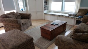 A living room with patterned furniture, a wooden coffee table, and a window seat with a checkered cushion.