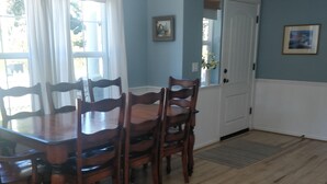A dining area with a wooden table and chairs, a white door, and a window with white curtains.