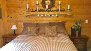 Une chambre confortable avec un mur en bois, un lit avec une literie à rayures, des coussins décoratifs, une table de chevet avec une lampe, une étagère avec des bougies et une couronne décorative.