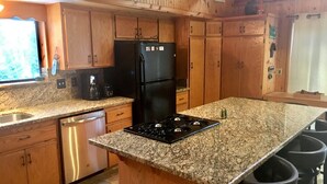 Une cuisine avec des meubles en bois, un réfrigérateur noir, un plan de travail en granit, un lave-vaisselle et une cuisinière à gaz.
