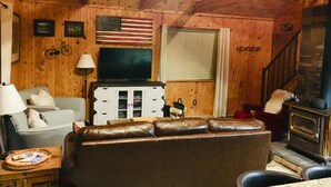 L’intérieur chaleureux d’un chalet avec un canapé en cuir, un téléviseur, une cheminée et des murs en bois.