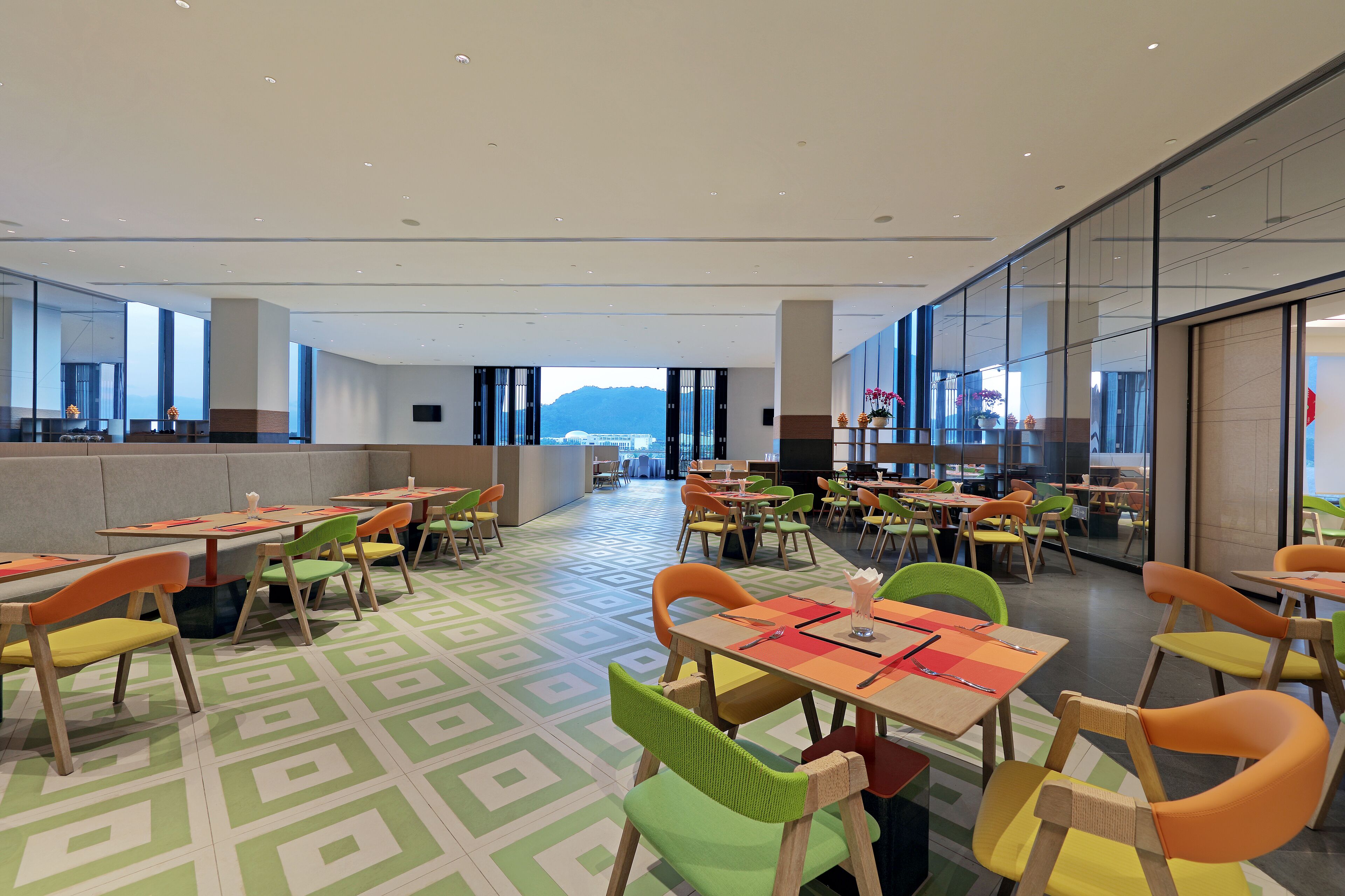A spacious dining area with multiple tables and chairs, large windows offering a view of the mountains, and a modern interior design.