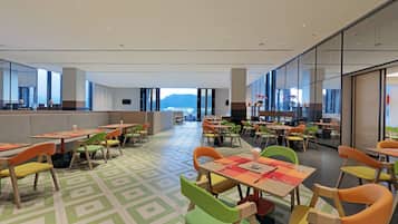 A spacious dining area with multiple tables and chairs, large windows offering a view of the mountains, and a modern interior design.
