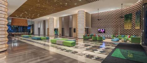 A spacious lobby with a checkered floor, green seating areas, and a modern ceiling design.