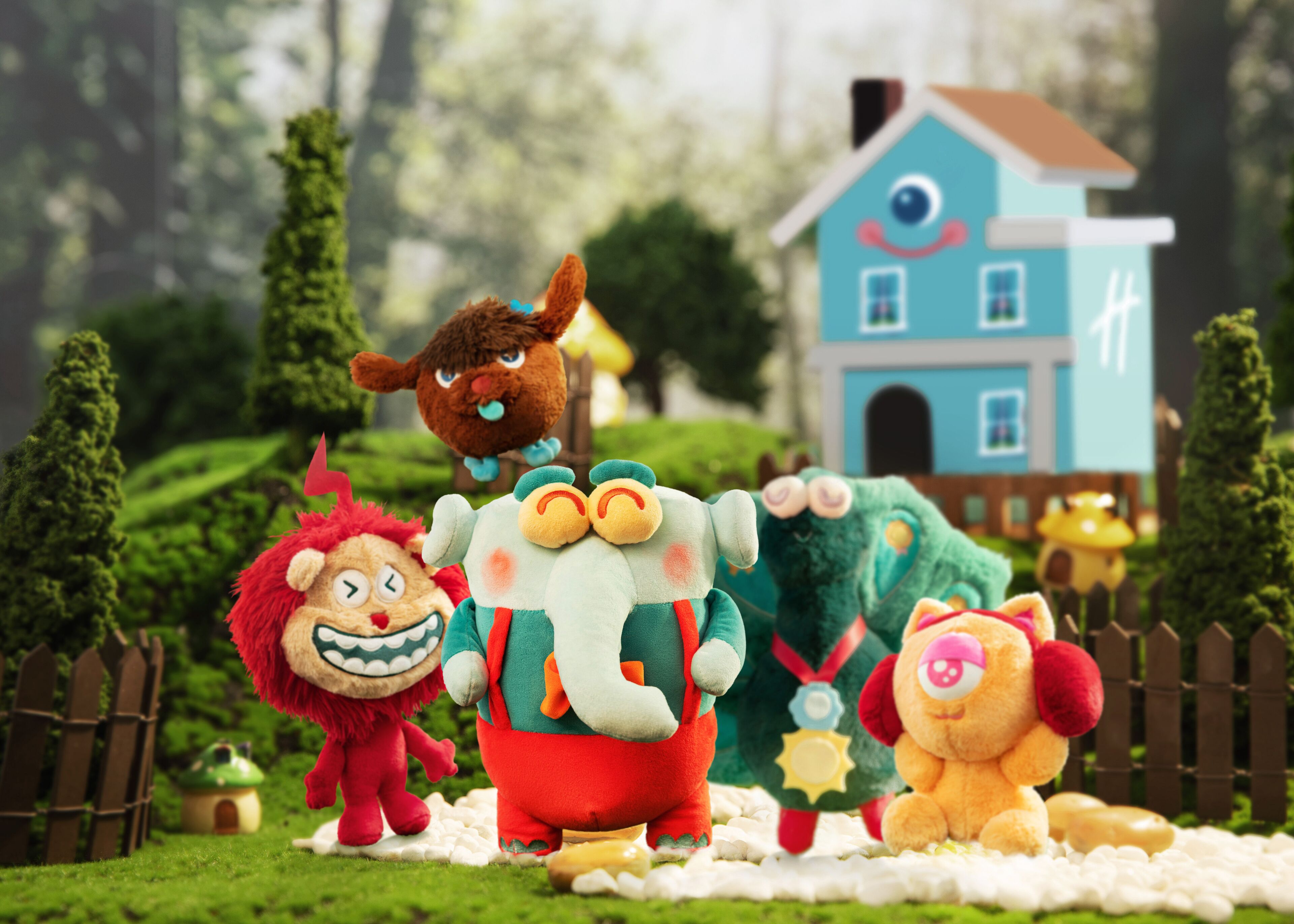Un grupo de juguetes suaves y coloridos en un jardín, con una casa al fondo.