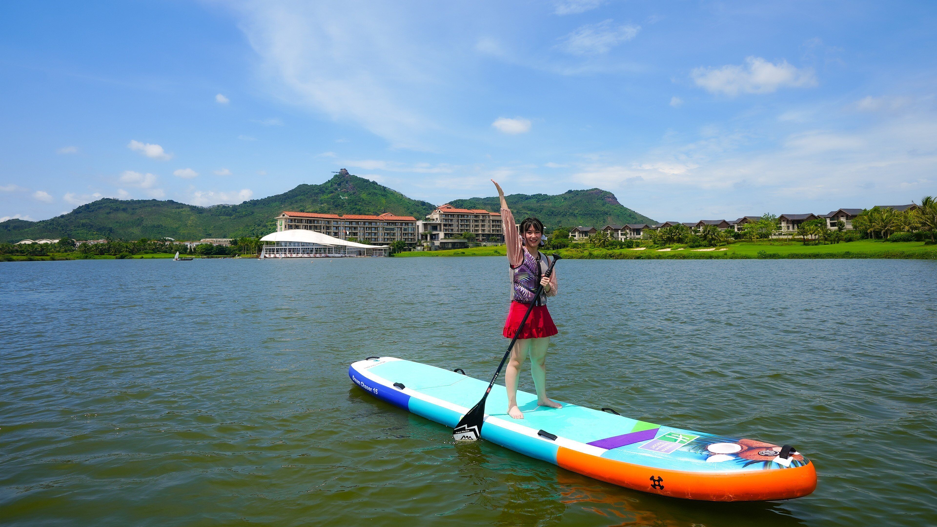 A person on a paddleboard in a body of water with a resort and buildings in the background.