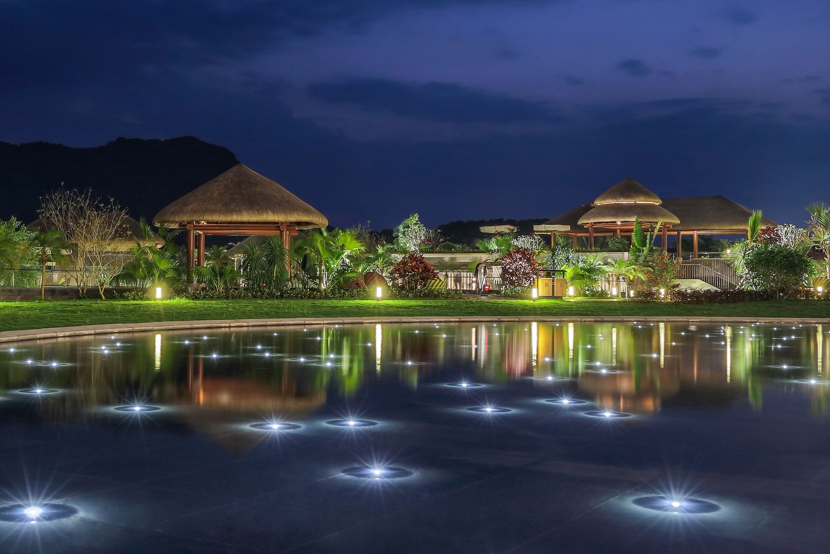 A resort with thatched-roof buildings, a reflective pool, and lush landscaping.