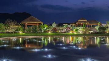 A resort with thatched-roof buildings, a reflective pool, and lush landscaping.