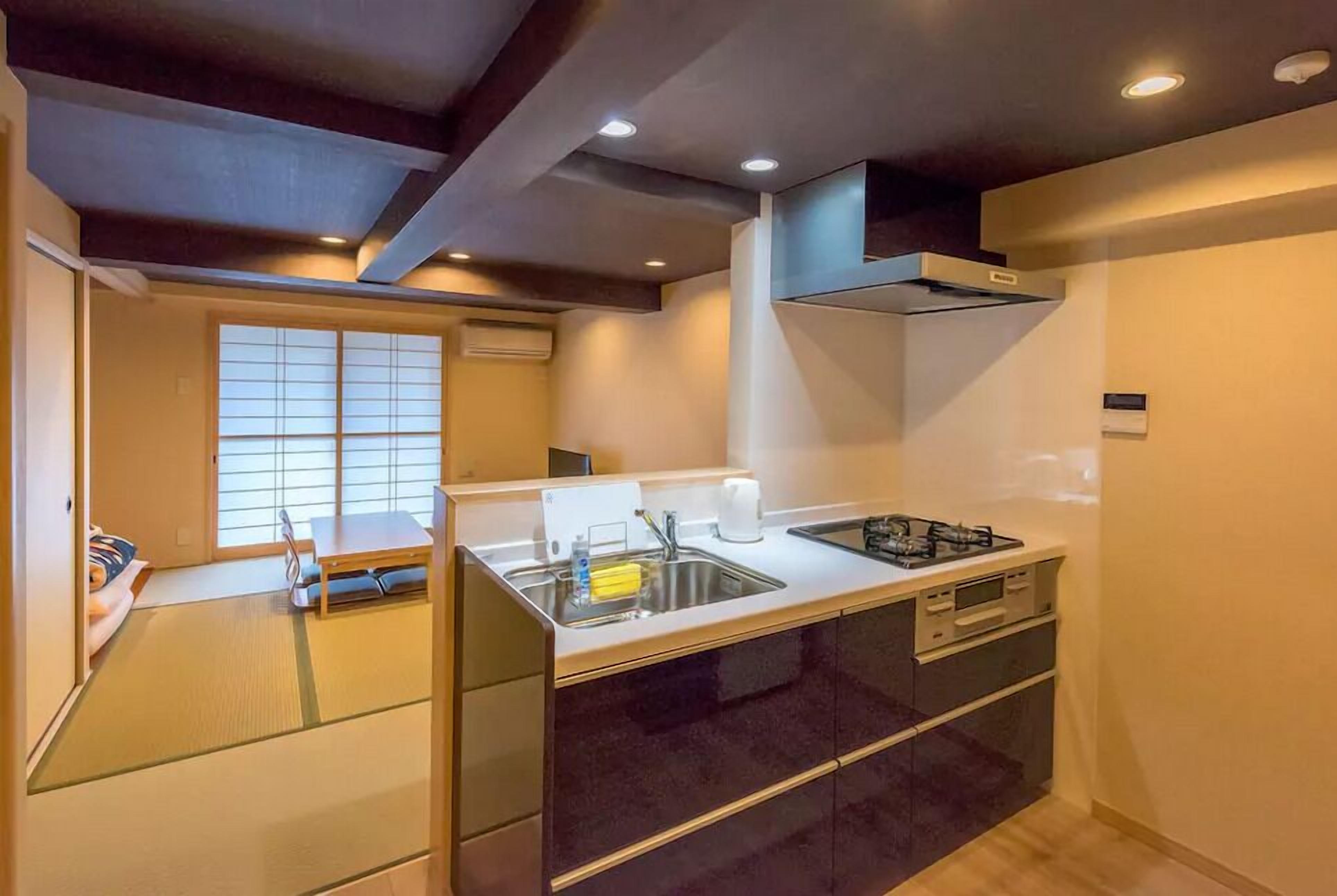 Una cocina compacta con lavamanos, estufa y armarios, una ventana con persianas y un techo con iluminación empotrada.