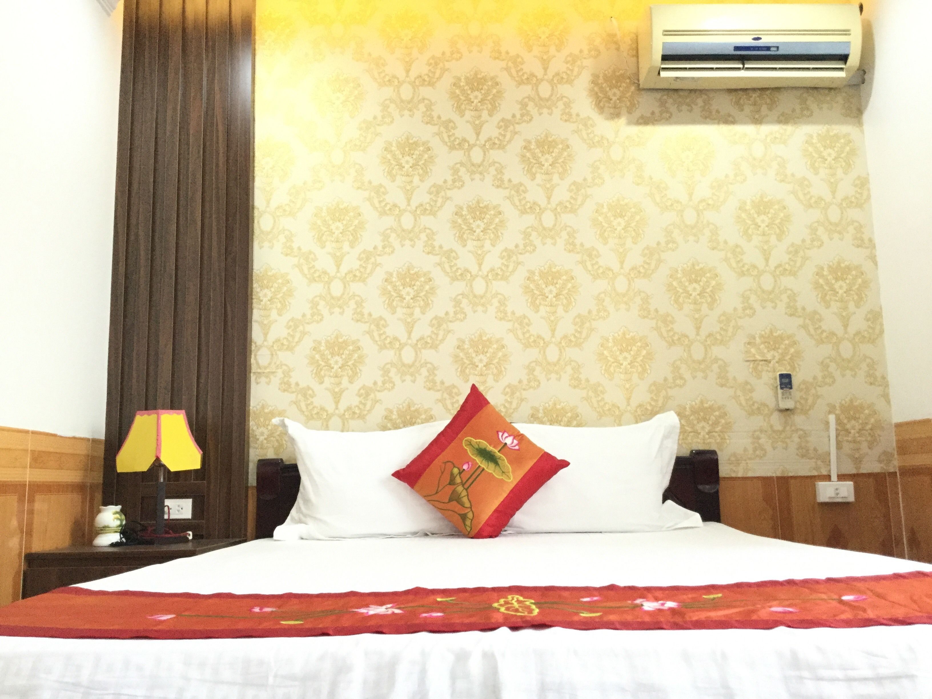 Habitación de hotel con cama, mesita de noche, lámpara, aire acondicionado y una pared con estampado floral.