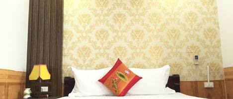 Habitación de hotel con cama, mesita de noche, lámpara, aire acondicionado y una pared con estampado floral.