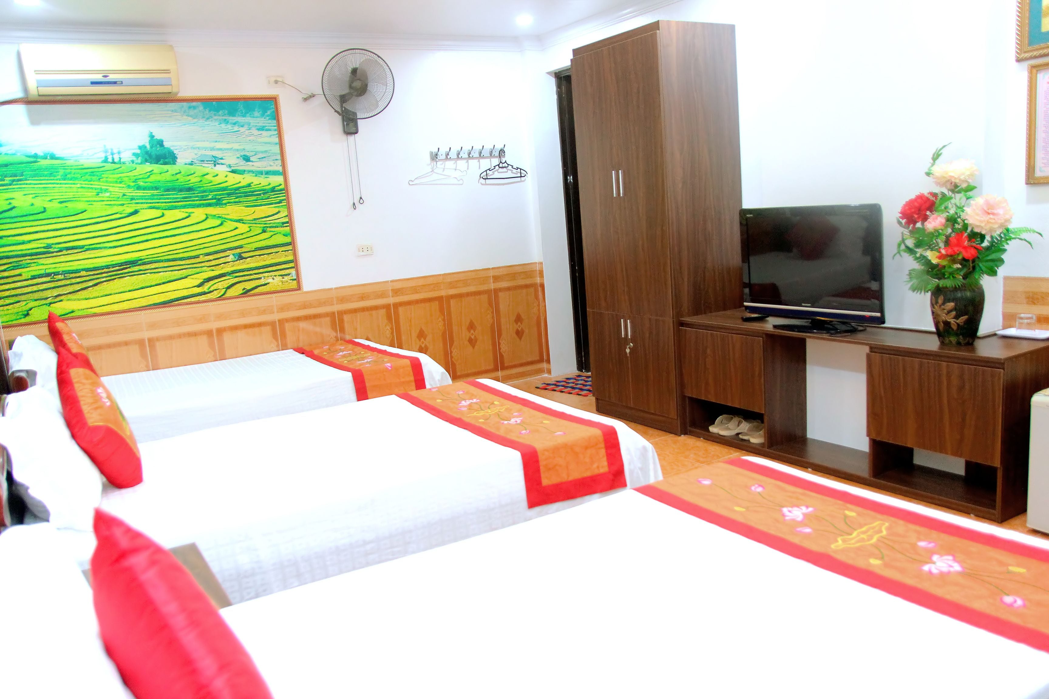 A hotel room with two beds, a TV, a wardrobe, and a painting on the wall.