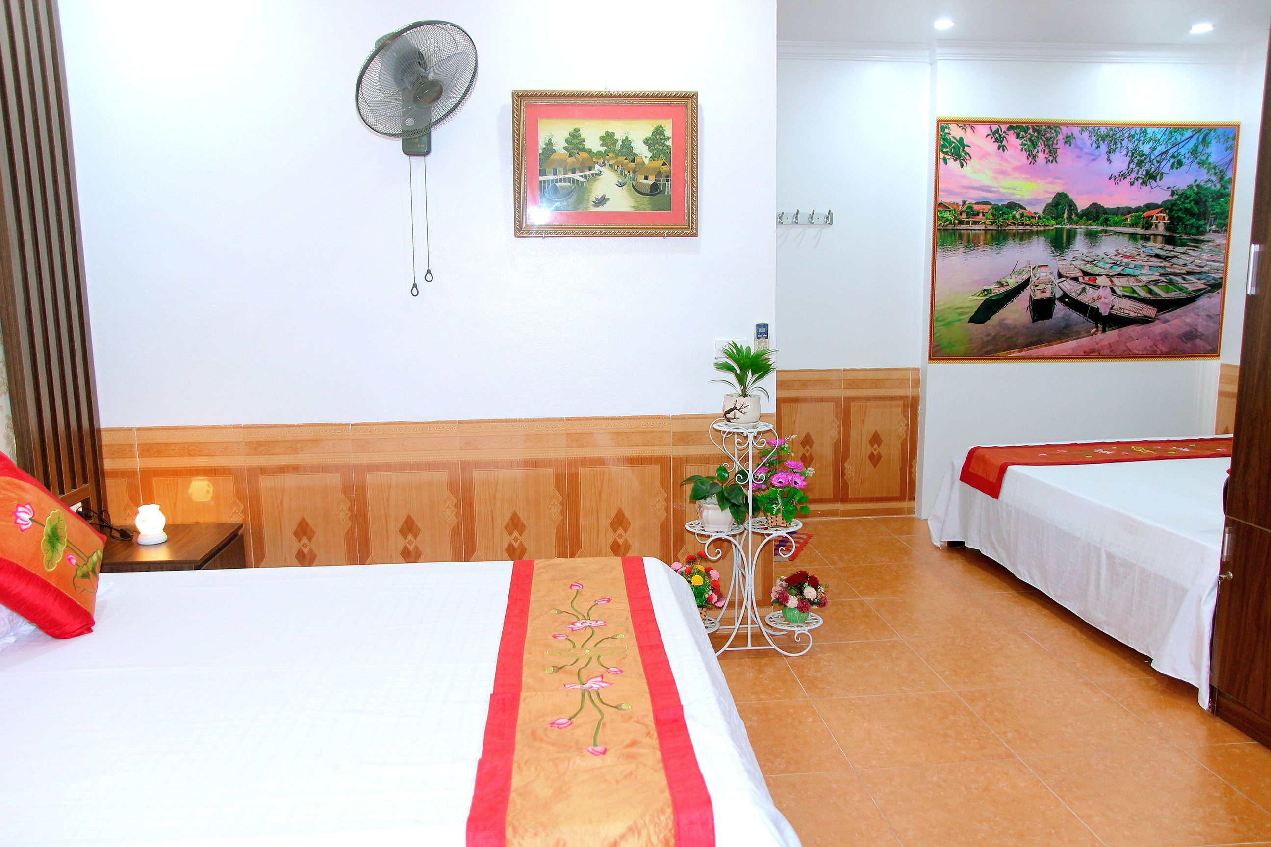 A hotel room with two beds, a wall-mounted fan, a framed painting, and a large window with a view of boats.