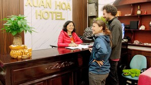 Mostrador de recepción en el Hotel Xuan Hoa con detalles de madera, una planta en maceta y una estatua de Buda.