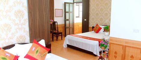 A hotel room with two beds, a desk, a chair, and a small table with a plant.