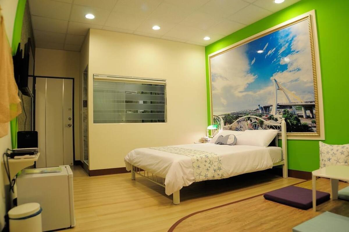 Een hotelkamer met een bed, een bureau, een stoel, een raam en een schilderij aan de muur.