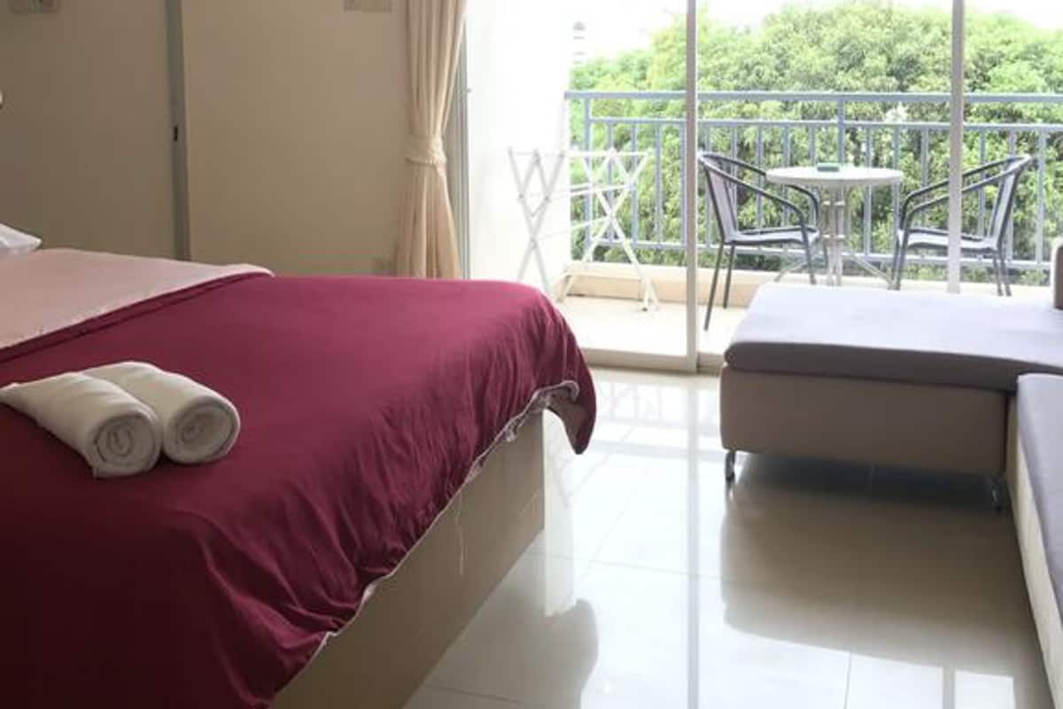 A hotel room with a bed, a balcony with a table and chairs, and an air conditioning unit.