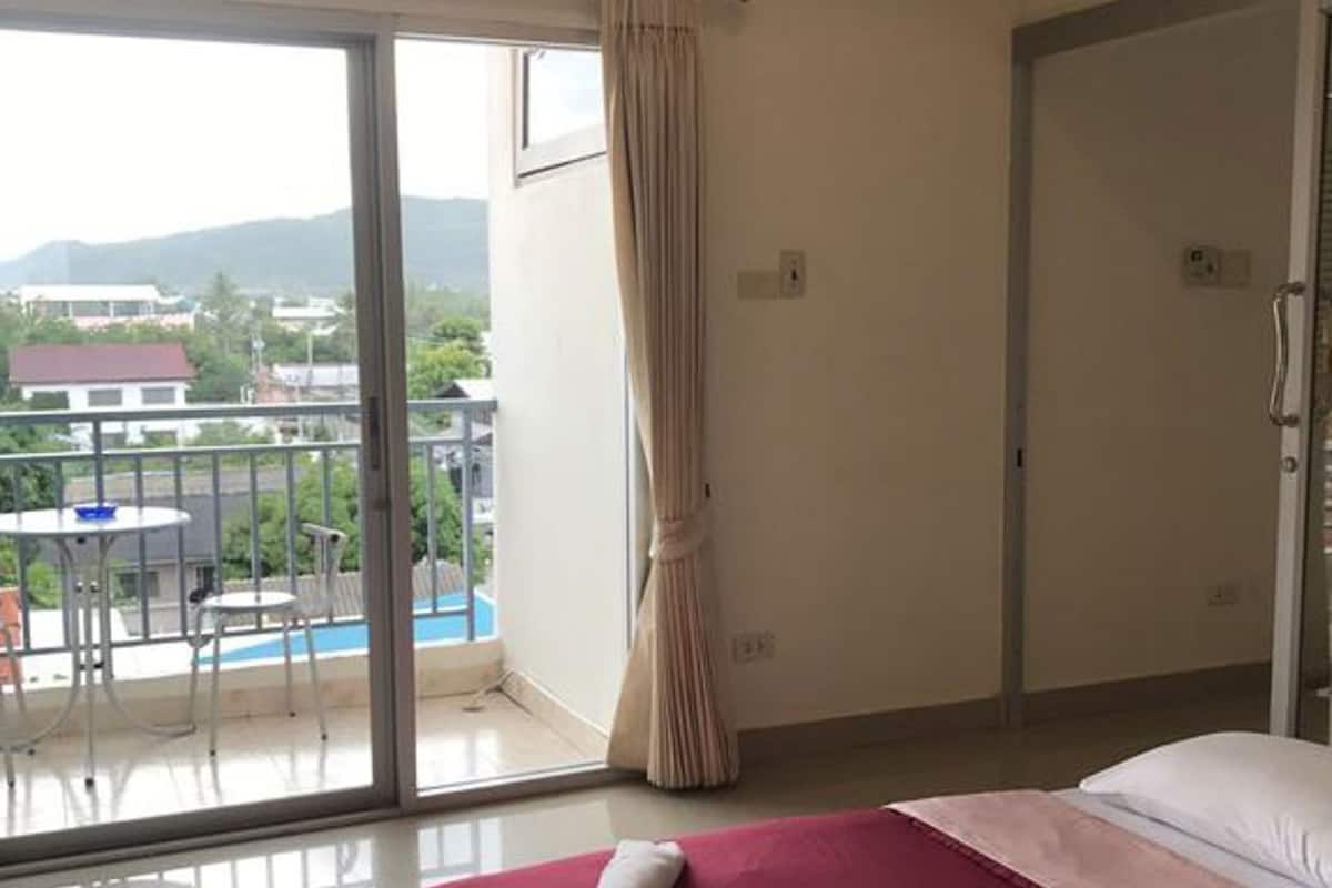 A hotel room with a bed, a window with a curtain, an air conditioning unit, and a view of a pool and buildings.
