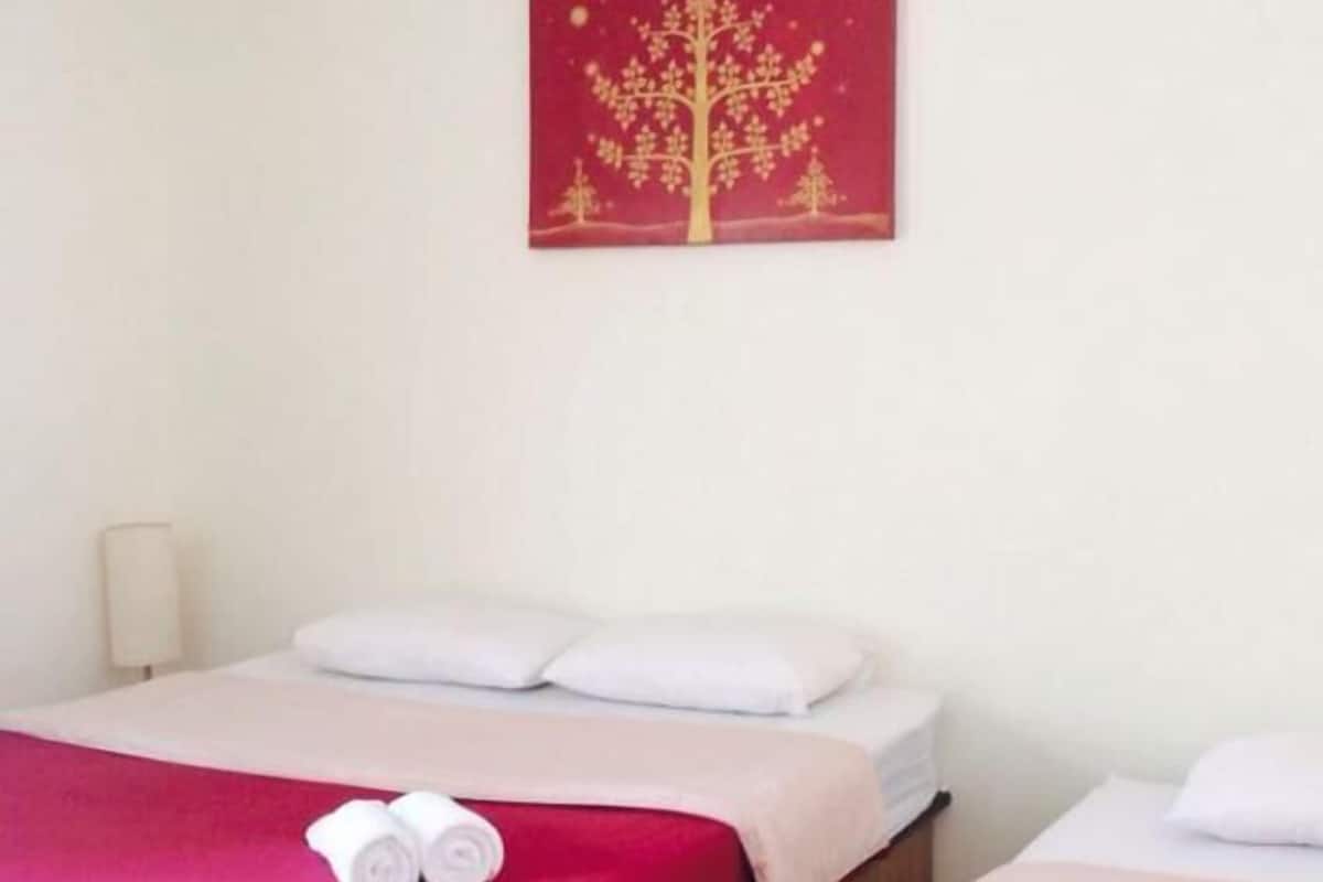 A hotel room with two beds, each with a red bedspread and white pillows. There is a painting of a tree on the wall above the beds.