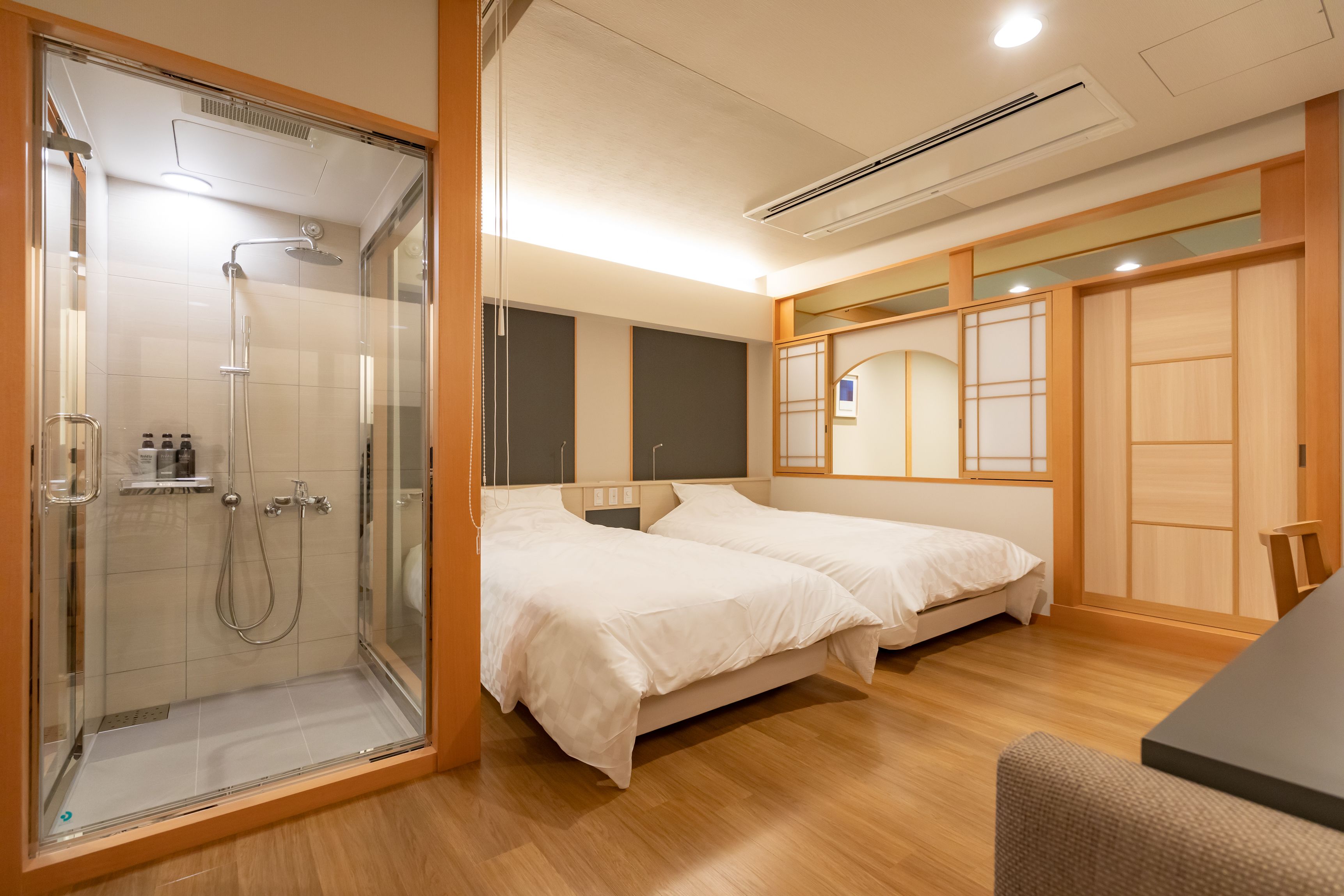 A hotel room with a glass-enclosed shower, two beds, a wooden floor, and a traditional Japanese sliding door.