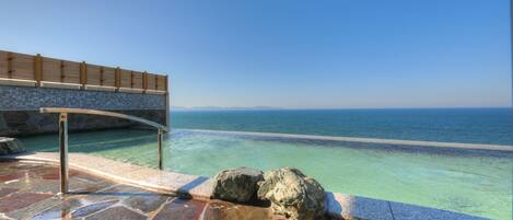 A stone pool with clear water, a wooden deck, and a view of the sea.
