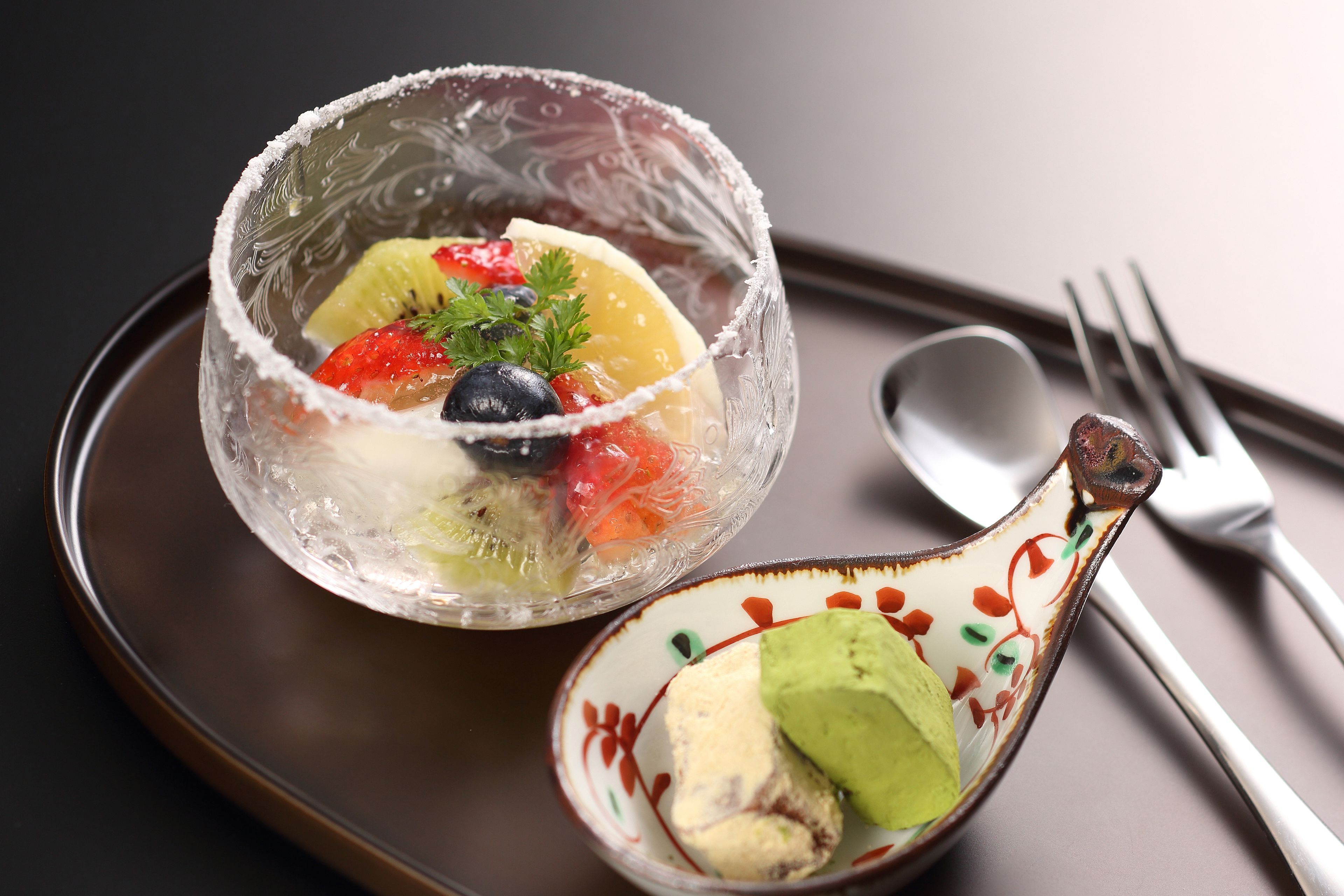 A dessert bowl with fruit and a spoon with ice cream.