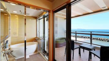 Une salle de bain moderne avec une douche à parois de verre et une baignoire, donnant sur un balcon équipé d’une table et de chaises, d’où l’on peut admirer la vue sur la plage.