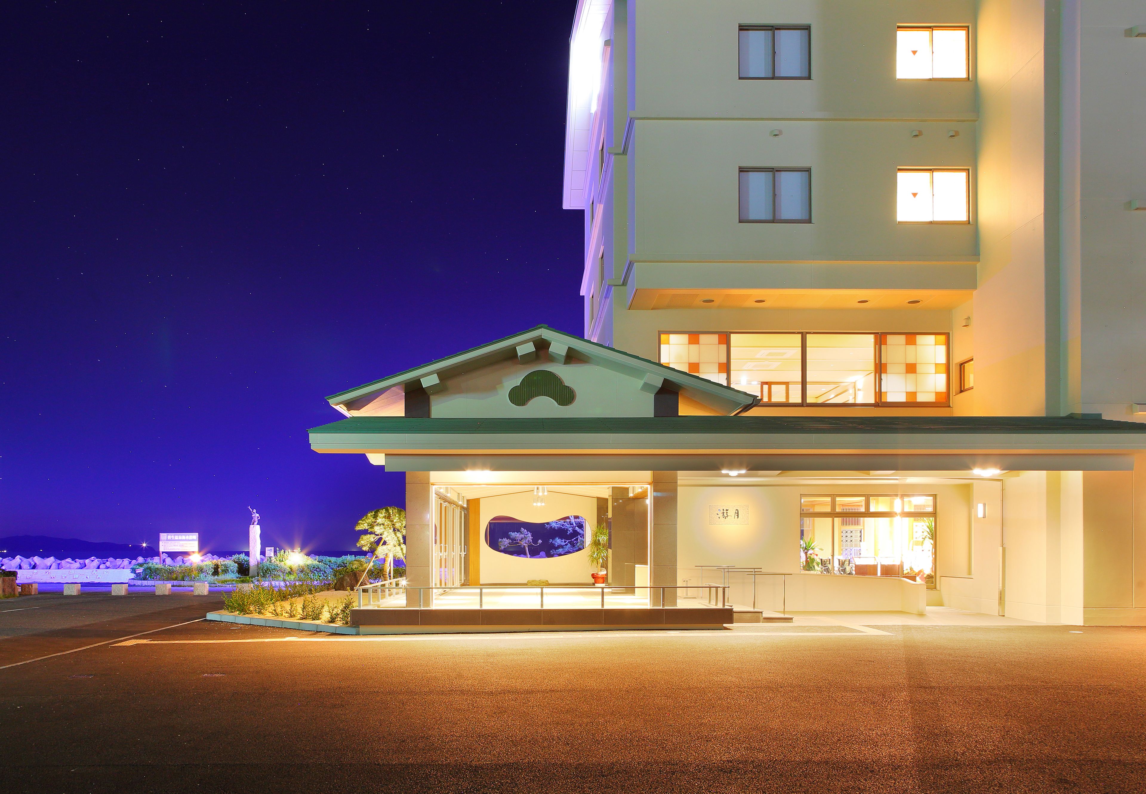 Ingresso di un hotel con un grande cartello illuminato, una statua e un'accoglienza ben illuminata.