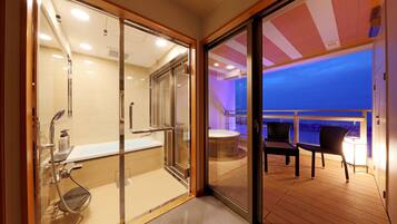 A modern bathroom with a glass shower enclosure, a bathtub, and a toilet. There is a wooden deck with two chairs and a table, and a view of the ocean.