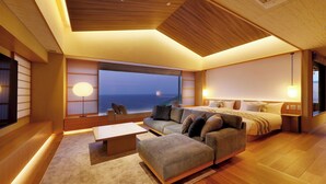 A modern living room with a sofa, ottoman, and a large window offering a view of the sea.