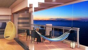 A balcony with a view of the sea at sunset, featuring a hanging chair, a hammock, and a table with chairs.