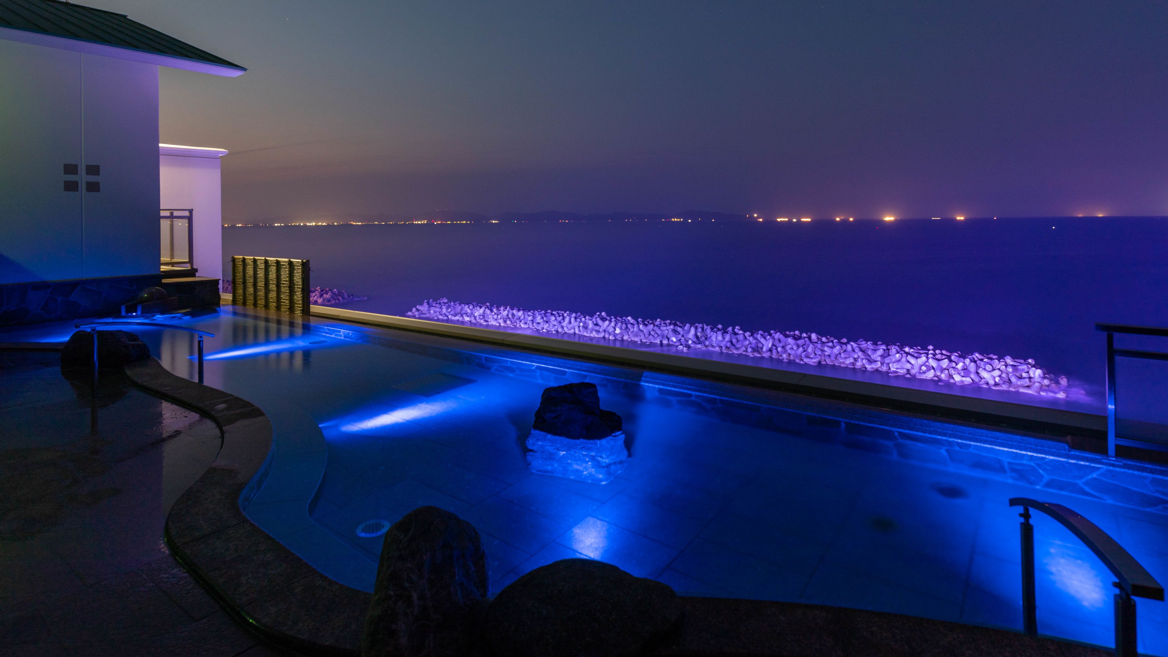 An infinity pool with a view of the ocean, a seating area, and a stone wall.