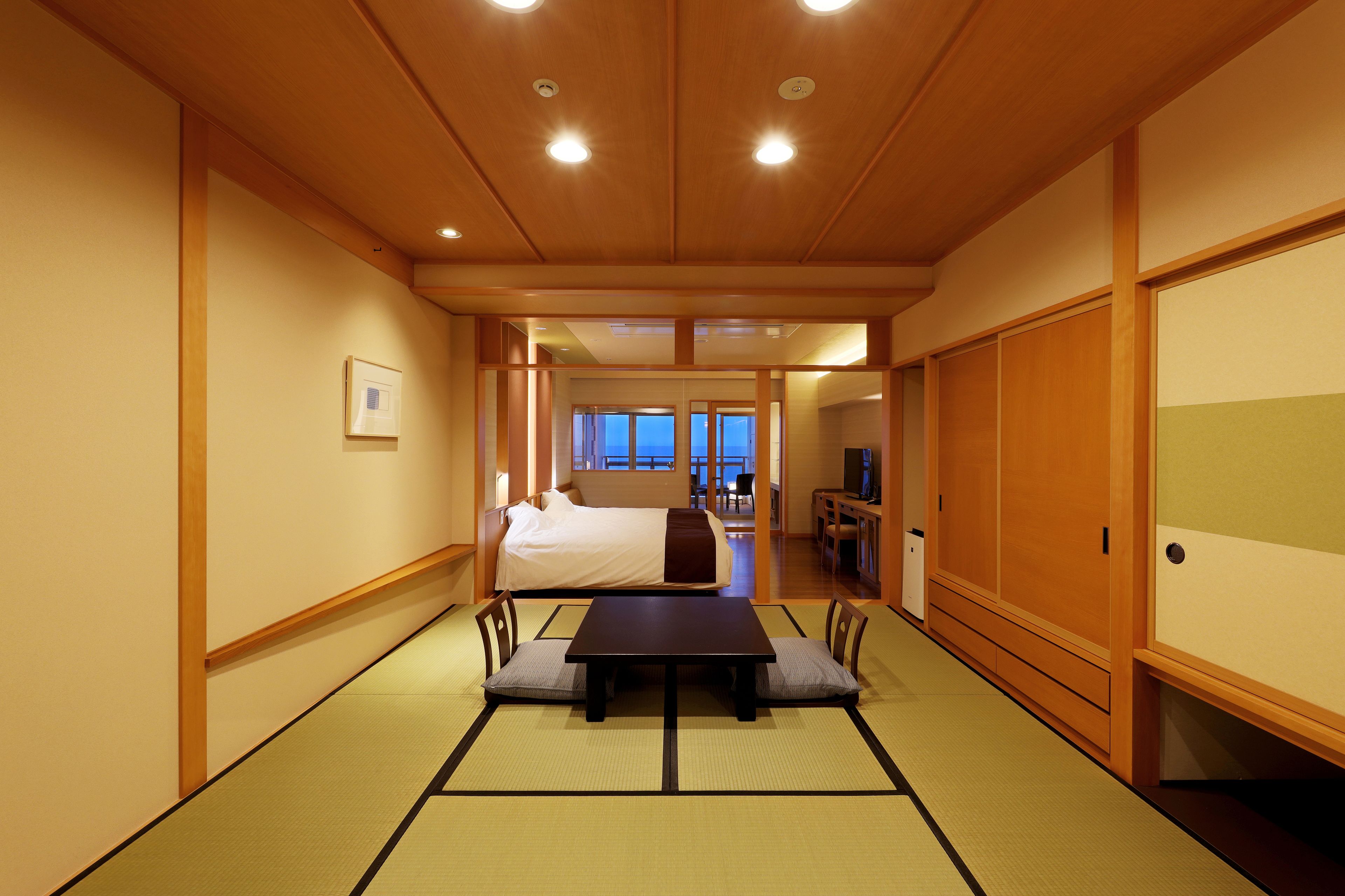 A traditional Japanese-style room with tatami flooring, a bed, a table with cushions, and sliding doors.
