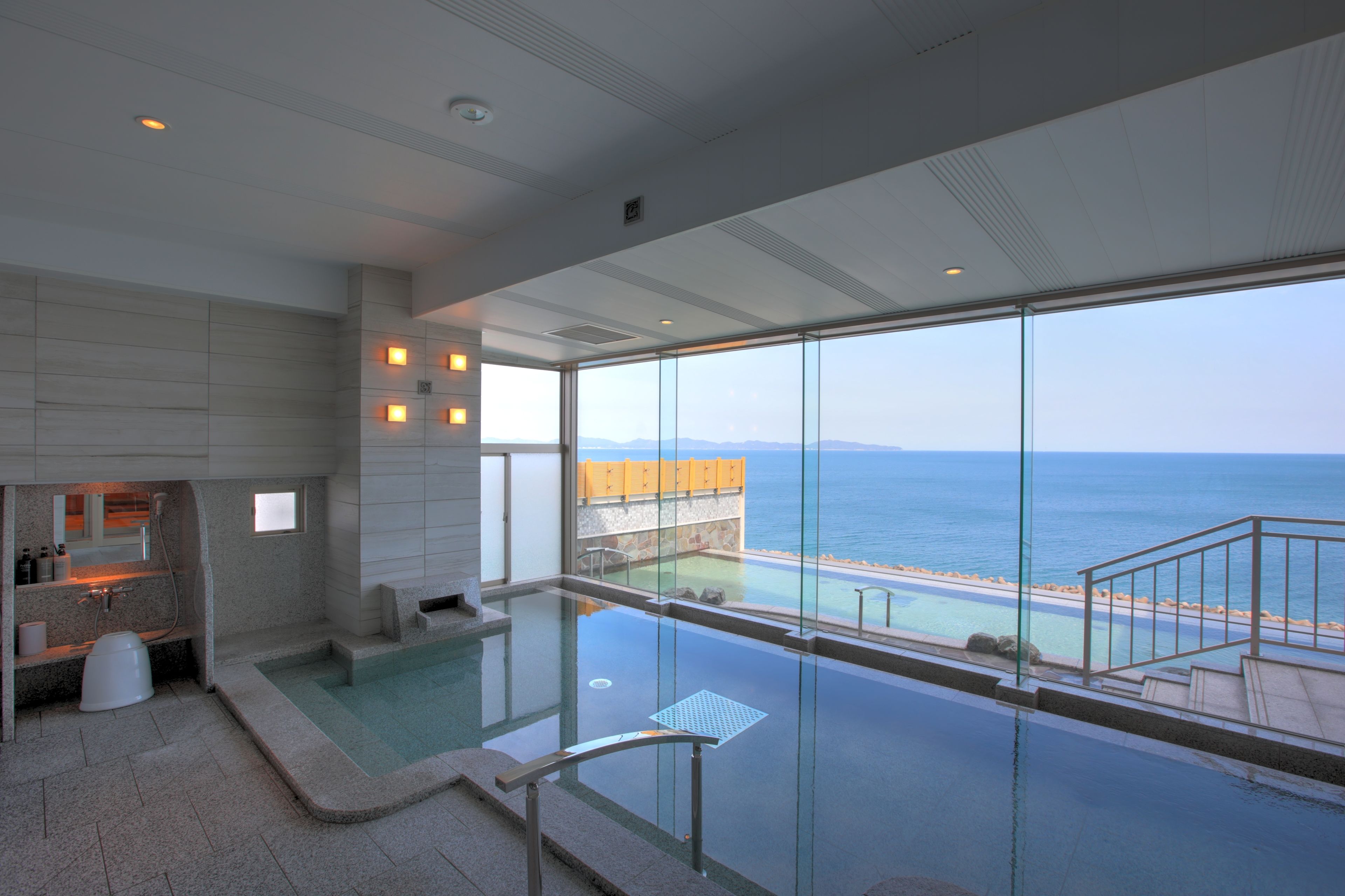 A modern hotel room with a large glass window overlooking a pool and the sea.