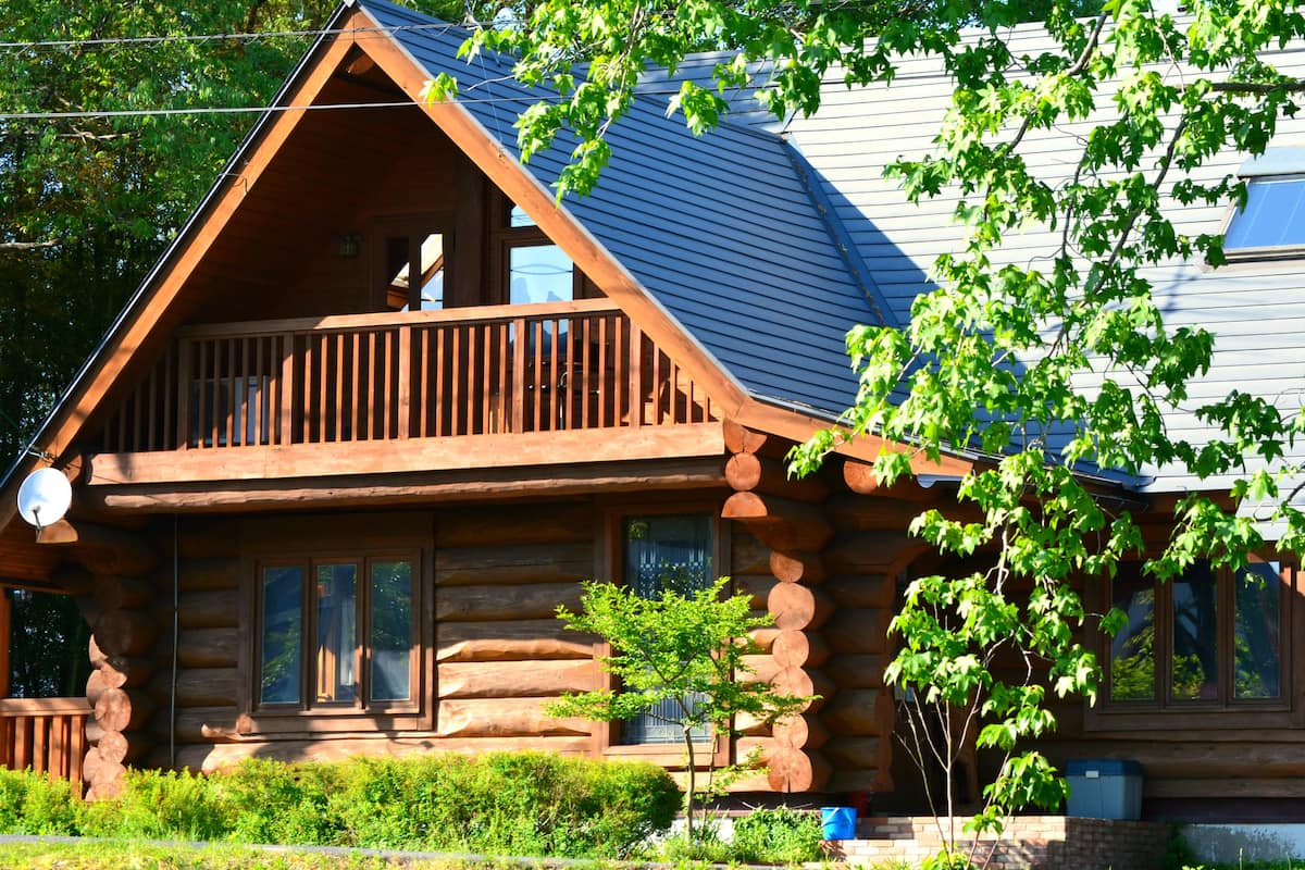 A log cabin with a balcony, large windows, and a chimney.