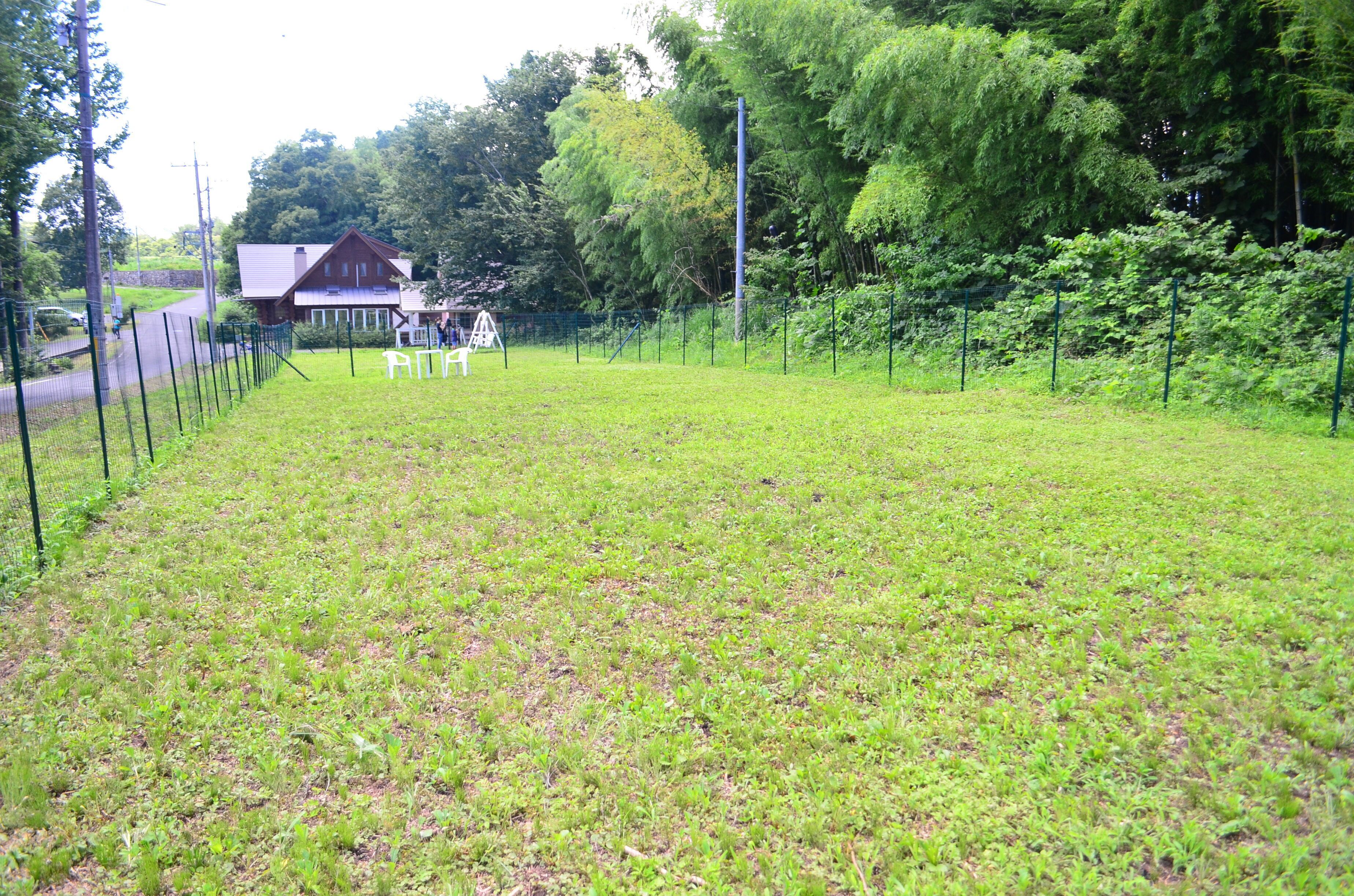 Un área verde cercada con un edificio de madera al fondo.