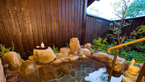 A stone hot spring with a wooden deck and a small bridge.