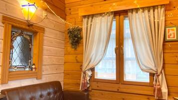 A cozy cabin interior with a leather sofa, wooden walls, a stained glass window, and curtains.