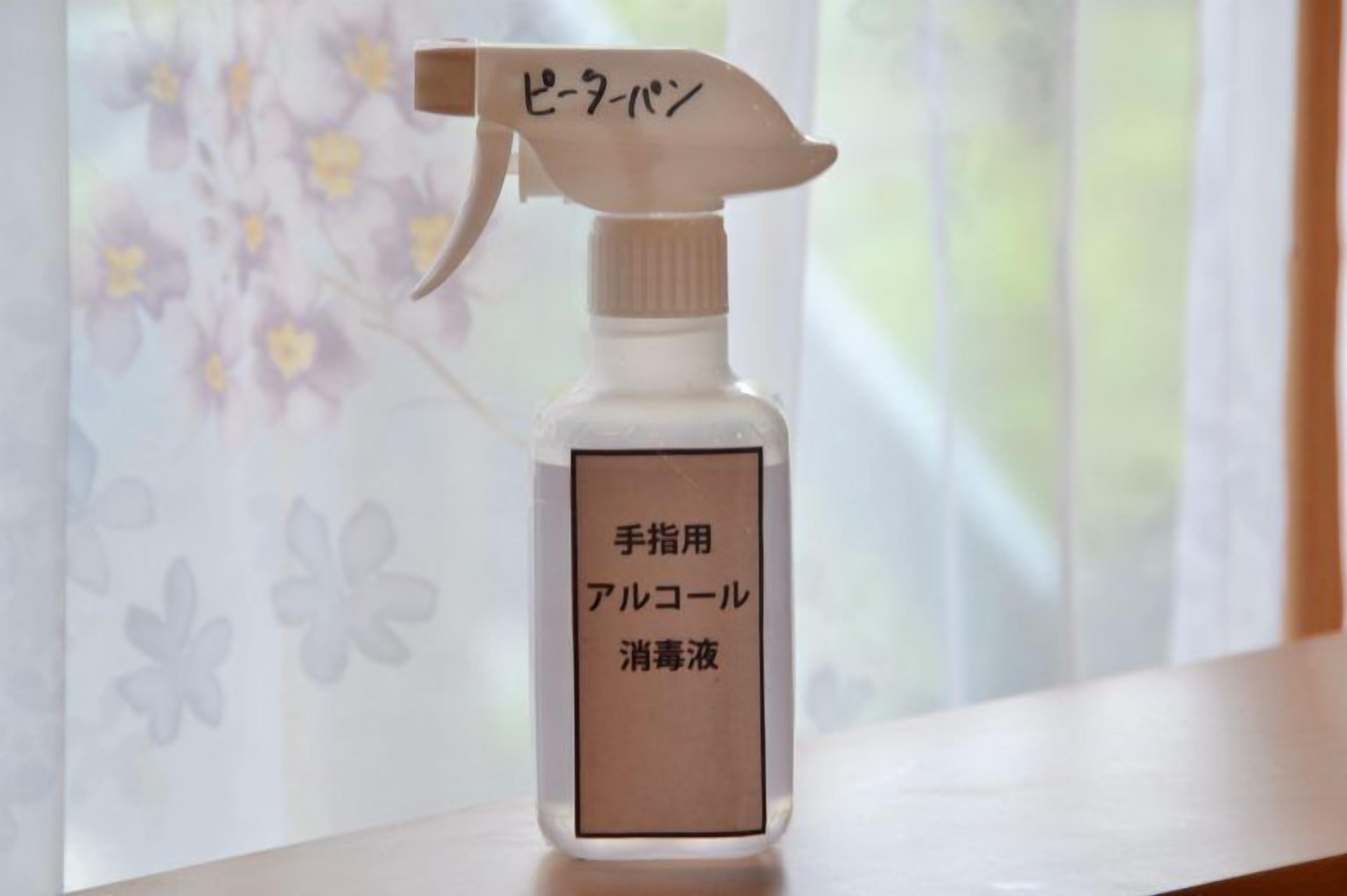 Un flacon pulvérisateur étiqueté « gel hydroalcoolique », avec un motif floral en arrière-plan.