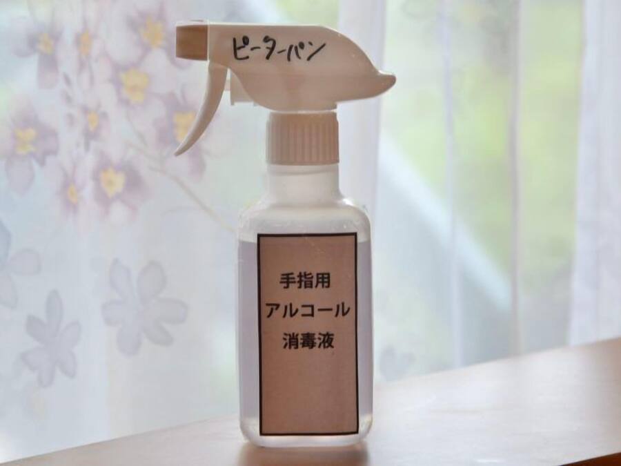 Un flacon pulvérisateur étiqueté « gel hydroalcoolique », avec un motif floral en arrière-plan.