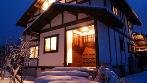 A traditional wooden house with a snow-covered entrance and a lit interior.