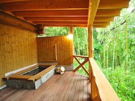 Terraza de madera con jacuzzi y cuenca de piedra, rodeada de abundante vegetación.