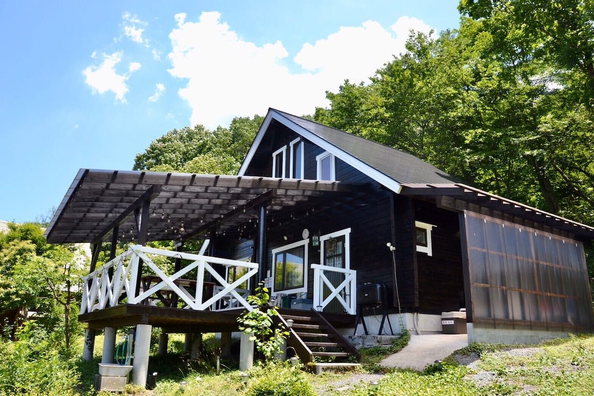 A rustic cabin with a wooden deck, a covered porch, and a metal extension.