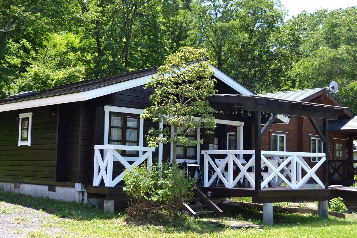 A cabin with a porch, a small tree, and a satellite dish.