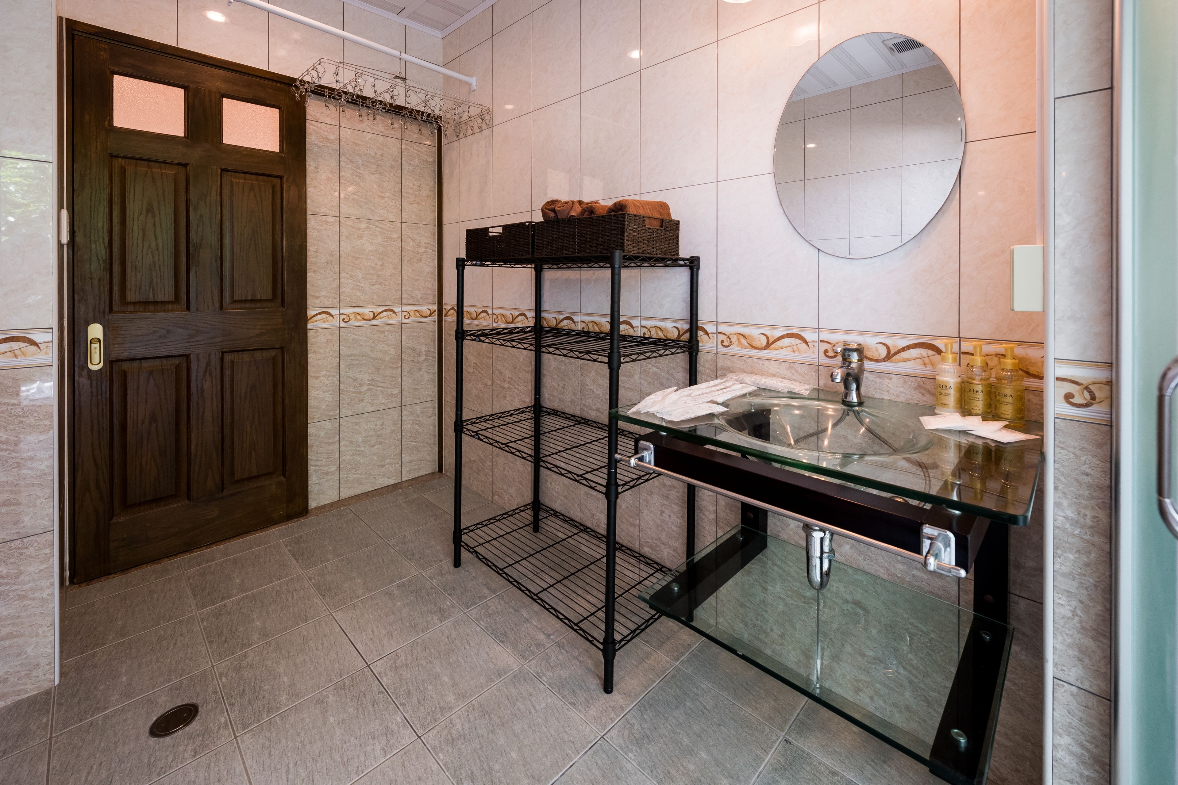 A bathroom with a wooden door, a glass sink, a mirror, and a metal shelf unit.